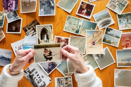 Woman holding a photograph in her hand with many photos spread on the table in front of her