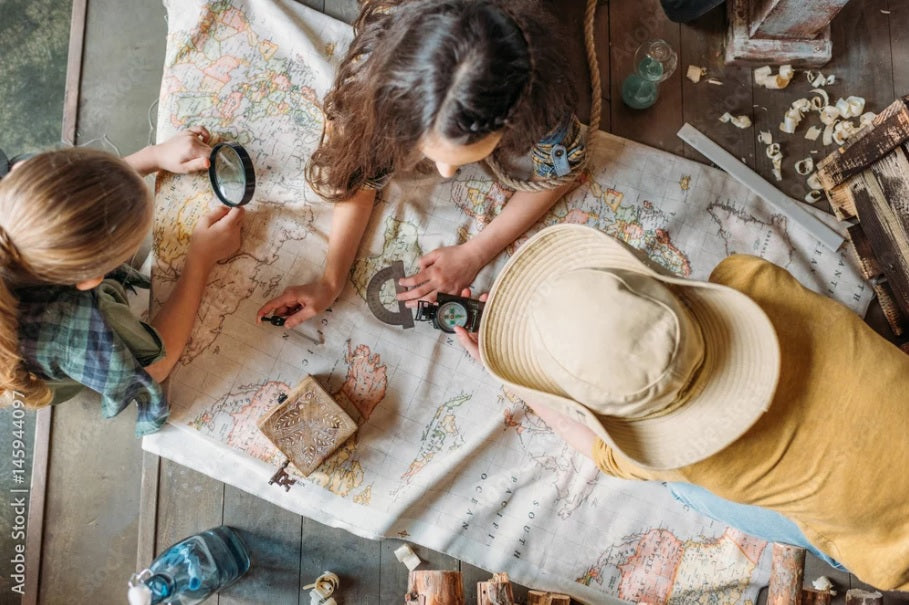 Three kids leaning over a world map on the floor, deciding where they want to travel to